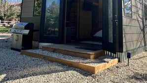 A modern two-story house with large sliding glass doors, a barbecue grill, and a gravel driveway. - "The Matador" Westcliffe Outpost Cabin  (Westcliffe)