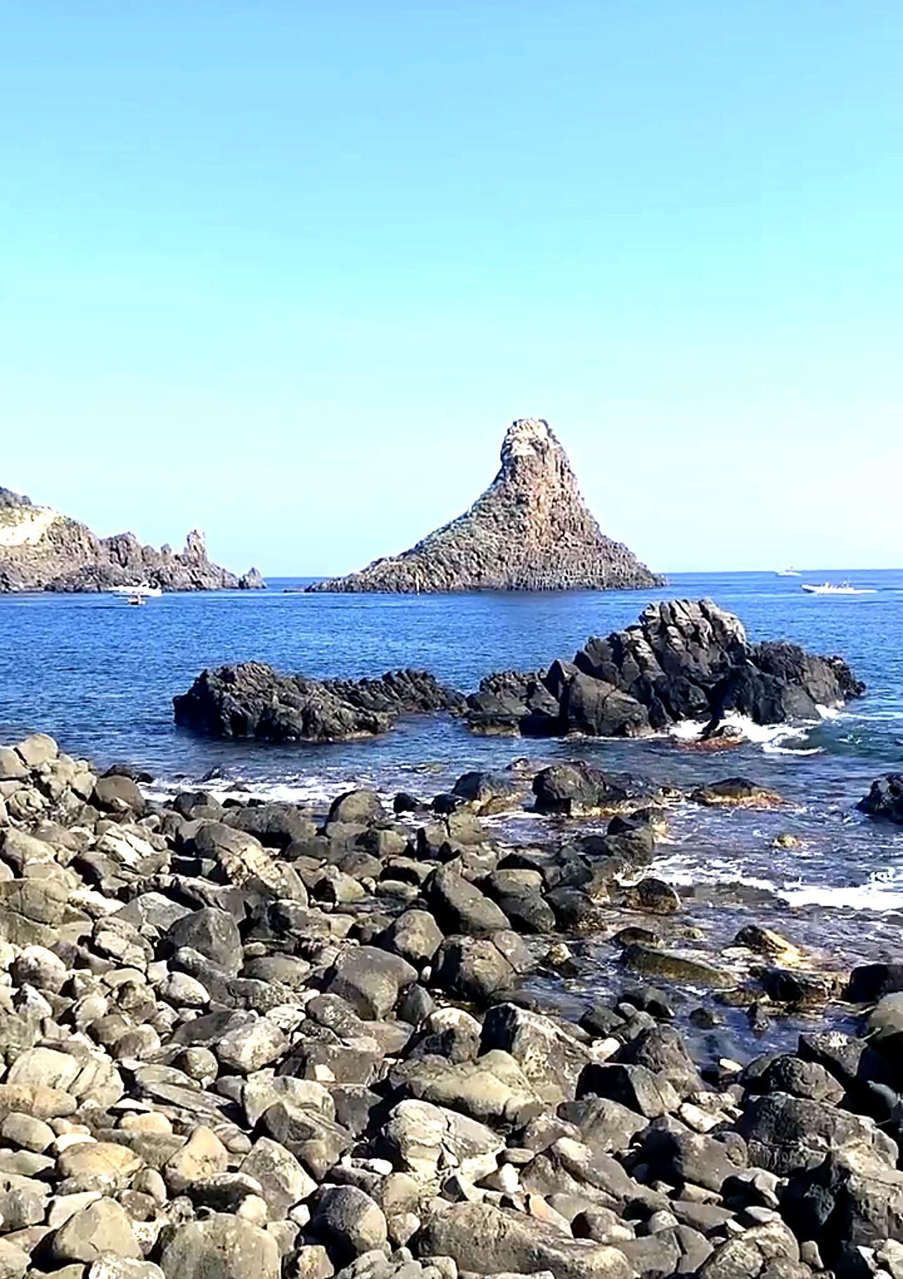 A rocky shoreline with large boulders and a prominent rock formation in the background.
