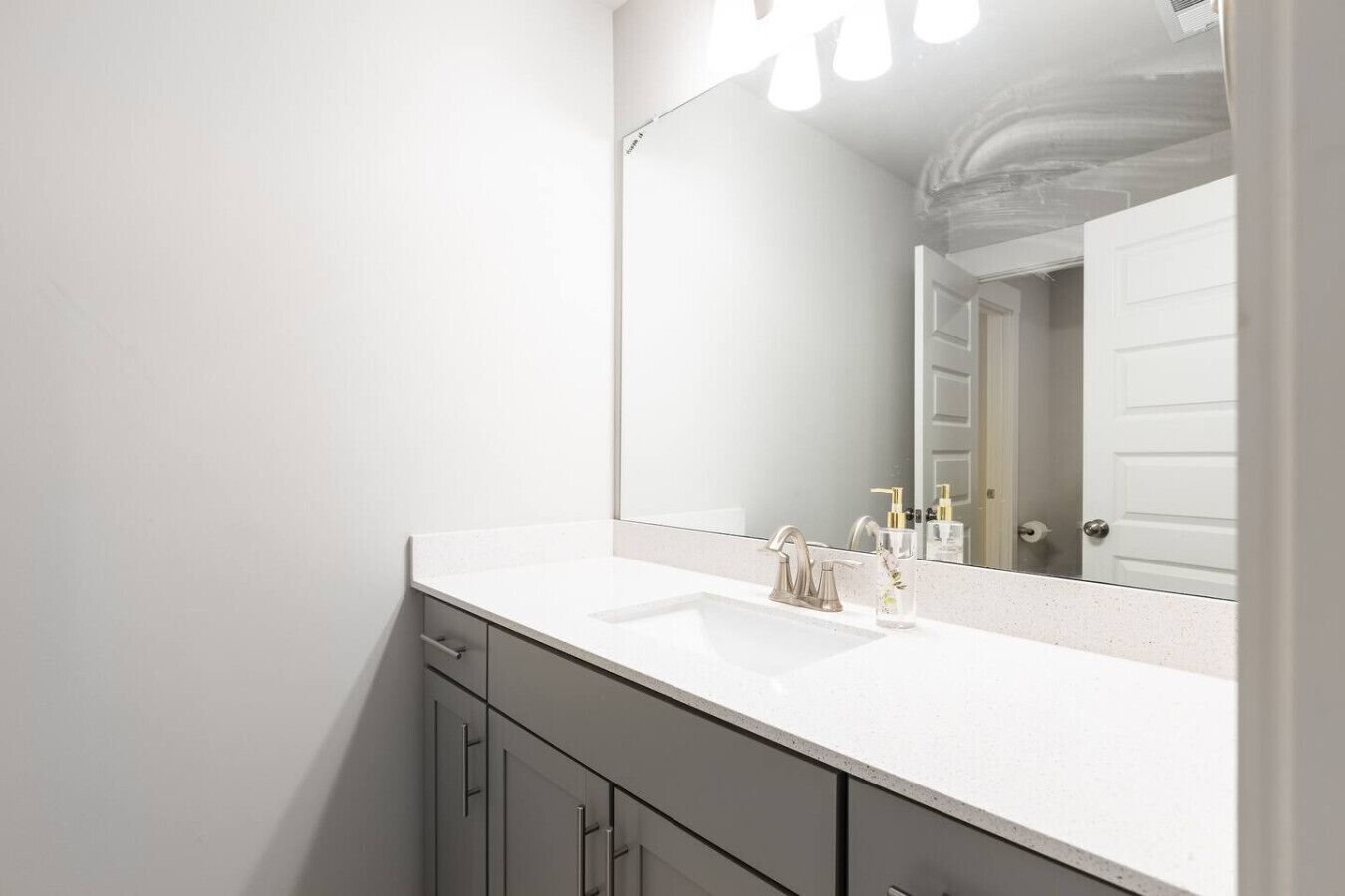 A modern bathroom with a white sink, a large mirror, and a door in the background.