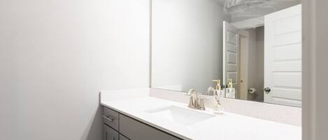 A modern bathroom with a white sink, a large mirror, and a door in the background.