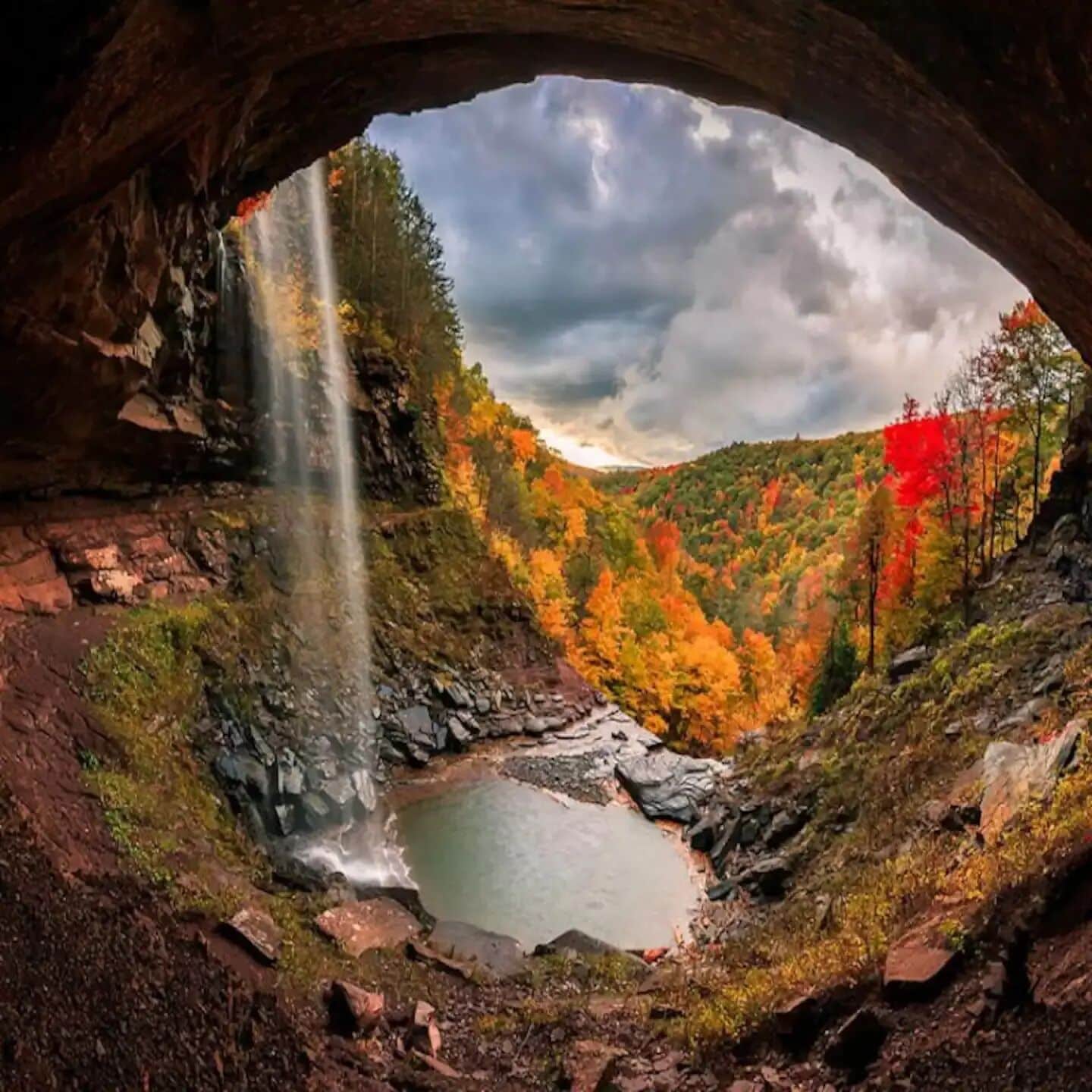 A waterfall cascading into a small lake surrounded by autumn foliage.