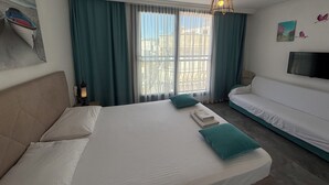 Ein Hotelzimmer mit Bett, Sofa, Fernseher und einem Fenster mit Vorhängen.