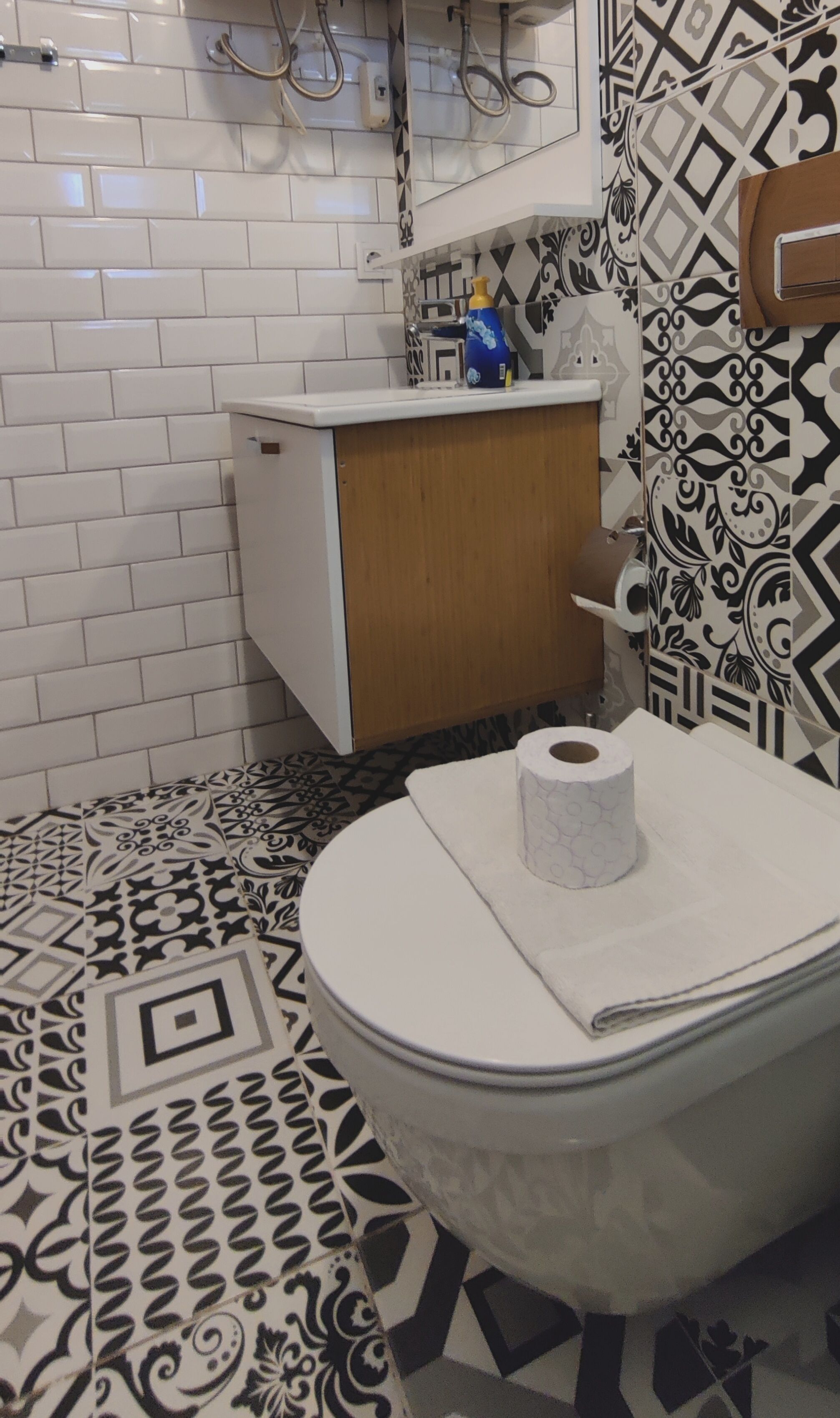 A bathroom with a white toilet, a wooden cabinet, and patterned floor tiles.