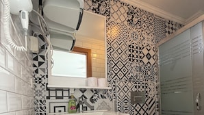 Ein Badezimmer mit einem weißen Waschbecken, einem Spiegel und einer Toilette. Die Wände sind mit einem schwarz-weißen geometrischen Muster gefliest.