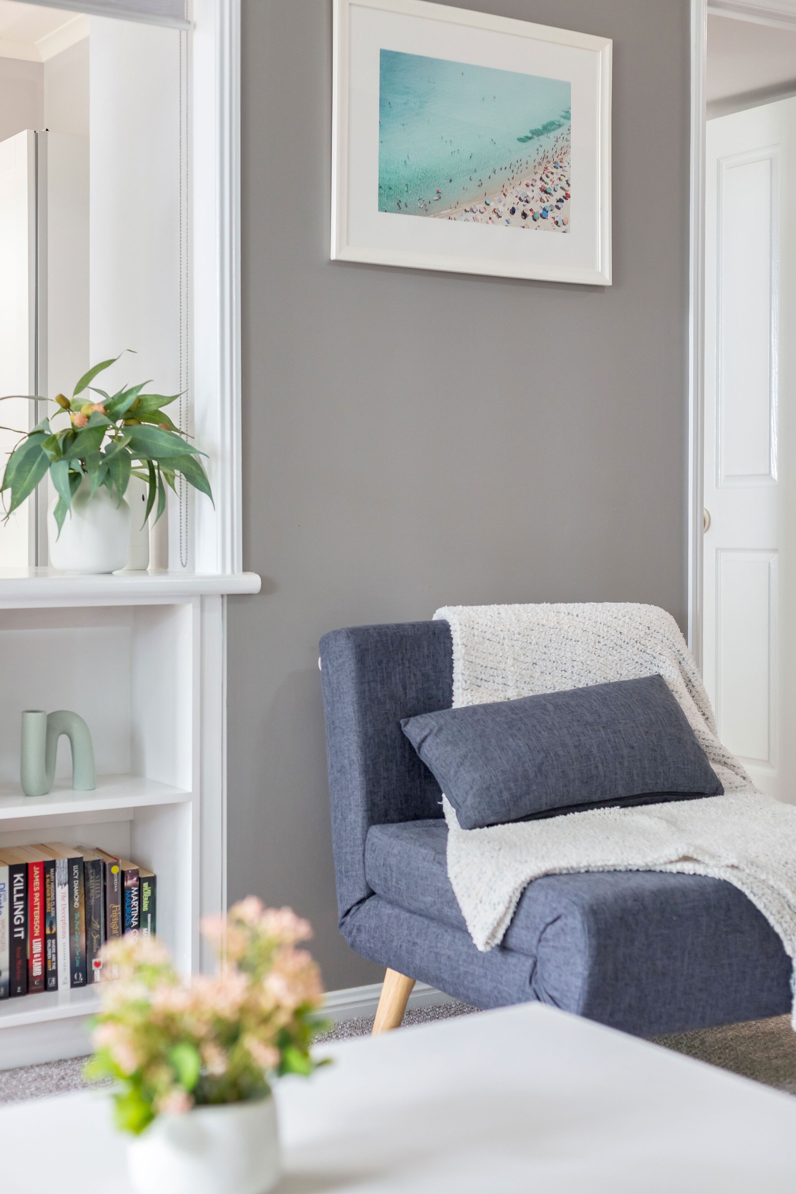 Una sala de estar moderna con un sillón gris, una mesa de centro blanca, una estantería y un cuadro enmarcado de una playa.