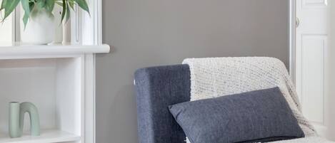Una sala de estar moderna con un sillón gris, una mesa de centro blanca, una estantería y un cuadro enmarcado de una playa.