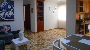 Un salon comprenant un canapé, une table basse et un coin repas avec une table et des chaises. Il y a également une cuisine équipée d’armoires et d’un évier.