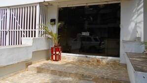 Une devanture de magasin avec une grande vitrine, une plante en pot et un véhicule garé à l’extérieur.