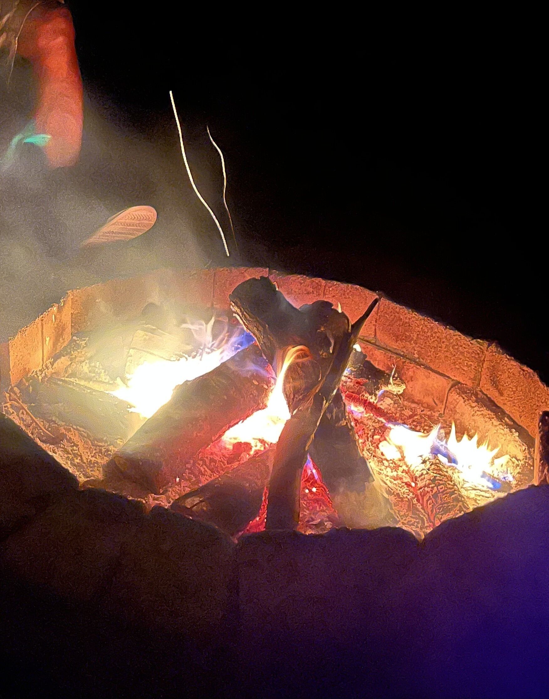 Una fogata en un brasero circular de piedra, con leña y brasas ardiendo.