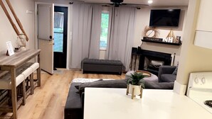 A modern living room with a fireplace, a television mounted above it, and a dining area with a table and bench. - Cozy condo in Waterville Valley NH.  (Waterville Valley)