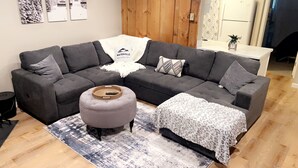 A modern living room with a grey sectional sofa, a round ottoman, and a patterned throw blanket. - Cozy condo in Waterville Valley NH.  (Waterville Valley)