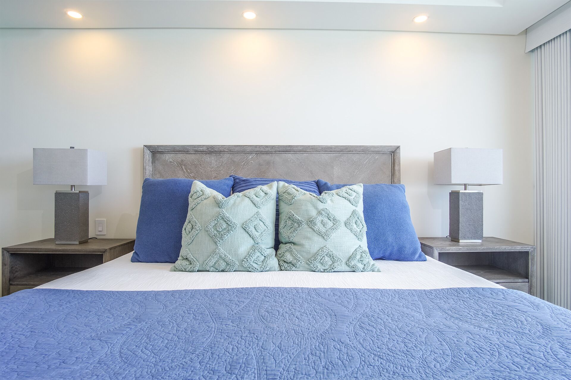Un lit bien fait, recouvert d’une couette bleue, avec deux tables de chevet dotées de lampes et une tête de lit.