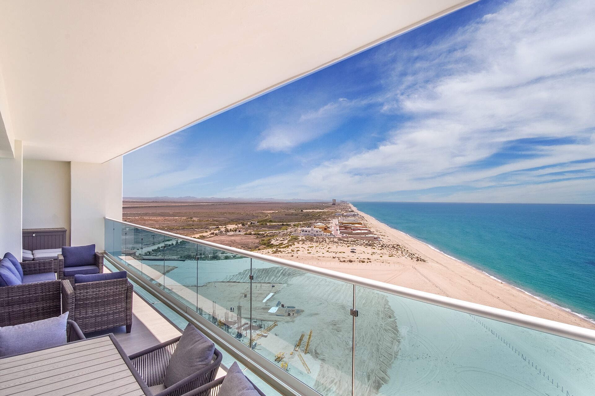 A balcony with a glass barrier overlooking a beach and ocean.
