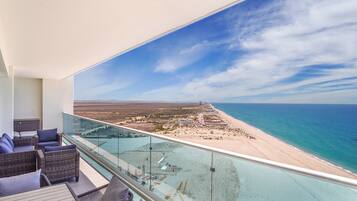 A balcony with a glass barrier overlooking a beach and ocean.