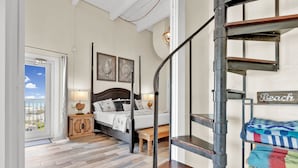 A bedroom with a wooden floor, a bed with a headboard, a nightstand, a lamp, and a view of the outside. - Penthouse Dahktari is a true beach front high-rise (10th floor) condominium (South Padre Island)