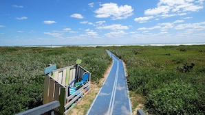 A pathway leading to a beach area with a wooden structure and a blue mat. - Penthouse Dahktari is a true beach front high-rise (10th floor) condominium (South Padre Island)