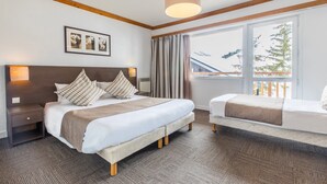 A hotel room with a large bed, a smaller bed, a nightstand, a lamp, a window with curtains, and a view of a mountain and trees.