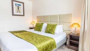 A neatly made bed with a green throw blanket and white bedding, two bedside lamps, and a framed picture on the wall.