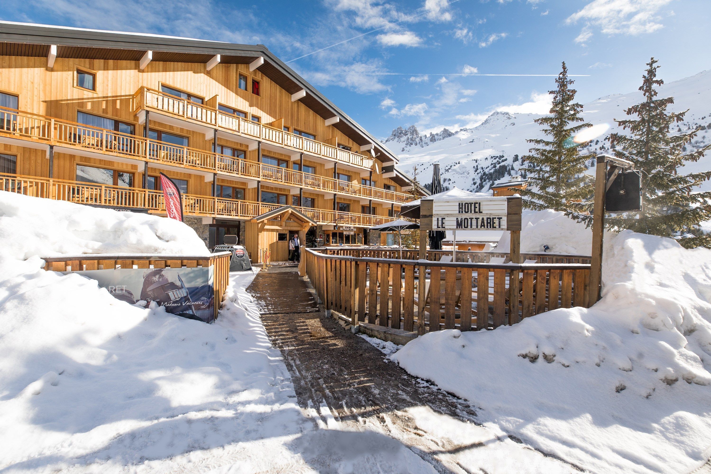 Ein hölzernes, mehrgeschossiges Hotel mit Balkonen, einer Skikanzel und einem verschneiten Berggrund.