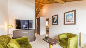 Ein modernes Wohnzimmer mit einem Flachbildfernseher, grünen Samsofas, einem kleinen Tisch und gerahmten Kunstwerken an den Wänden.