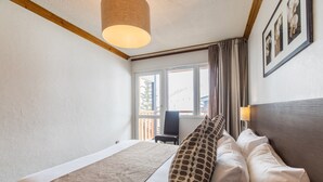 Une chambre d’hôtel avec un lit, une chaise, une fenêtre avec des rideaux et une lampe fixée au mur.