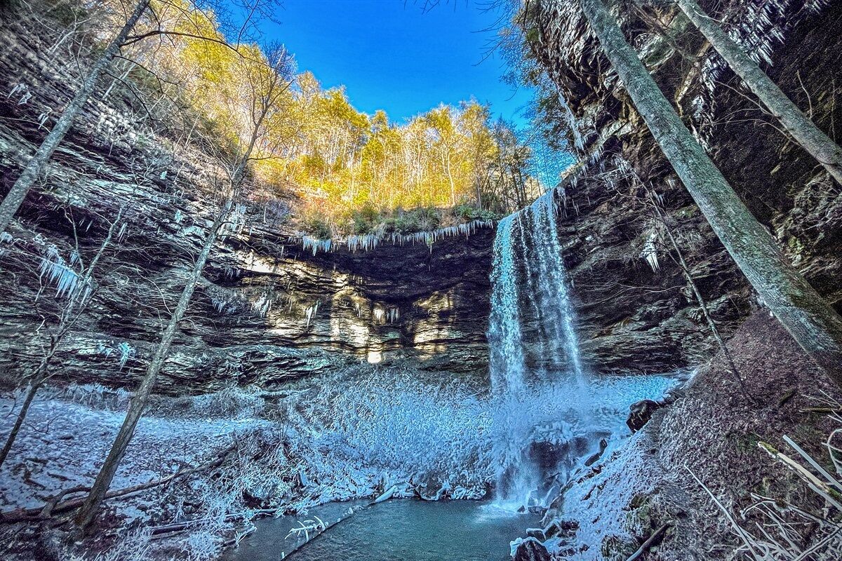 Ein Wasserfall in bewaldeter Landschaft mit Bäumen und felsigem Gelände.