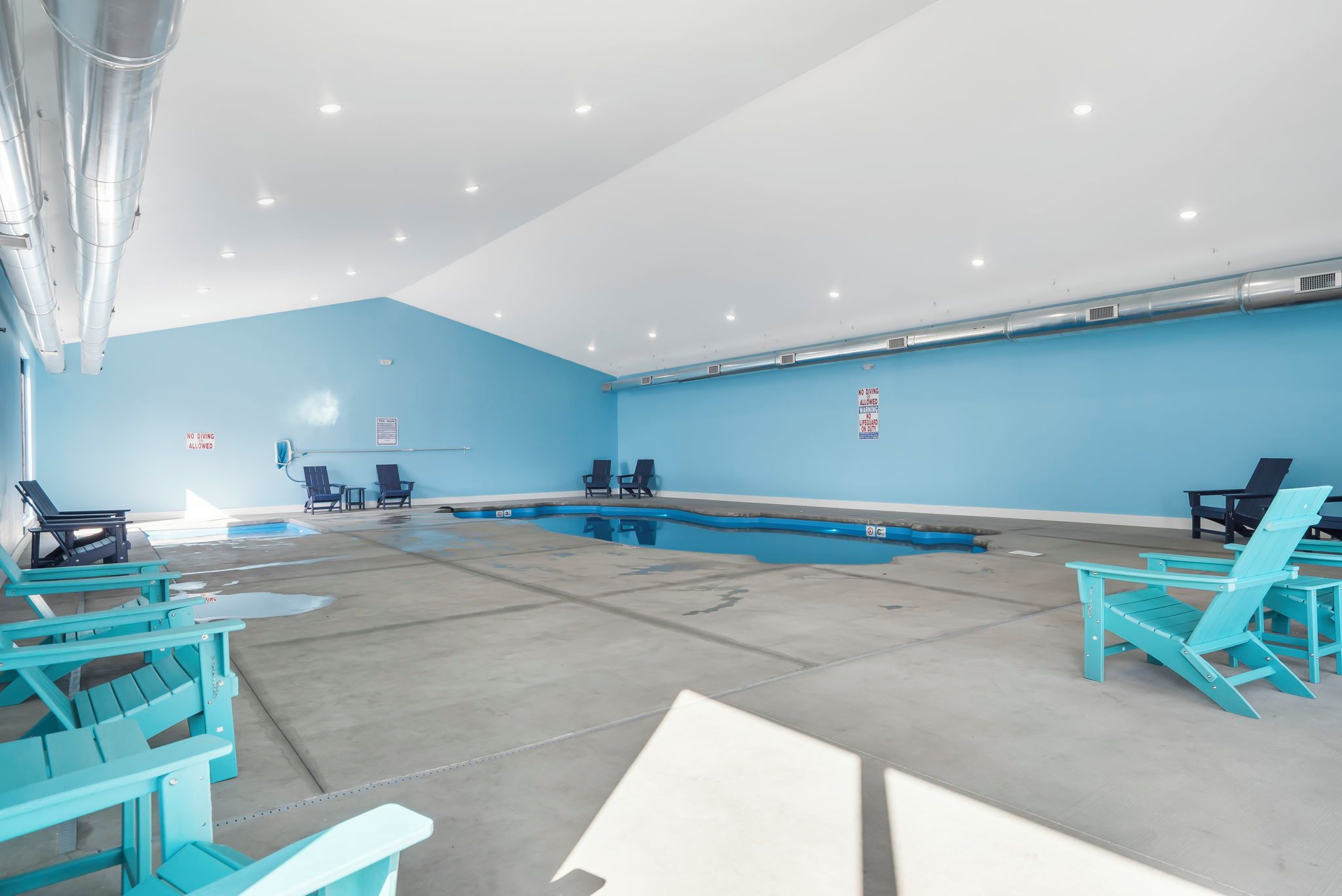 Un área de piscina con paredes azules, piso de concreto y varias sillas turquesa.