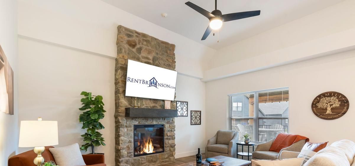 Ein Wohnzimmer mit Kamin aus Stein, Deckenventilator und einem Schild für RentBrinson.com.