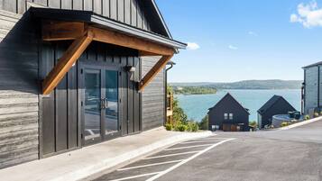 Un bâtiment doté d’une grande porte vitrée, d’un espace de stationnement avec des places délimitées et offrant une vue sur un lac où naviguent des bateaux.