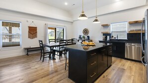 Une cuisine moderne dotée d’un îlot central, de meubles de rangement noirs, d’appareils électroménagers en acier inoxydable et d’un revêtement de sol en bois.