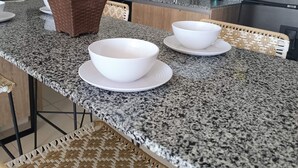 Una cocina con encimeras de granito, una isla central con un cuenco blanco, una planta en maceta y un refrigerador de acero inoxidable.