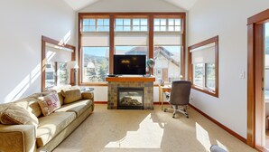 A living room with a fireplace, a sofa, a TV, and large windows. - Settler's Crossing #42 (Sun Peaks)