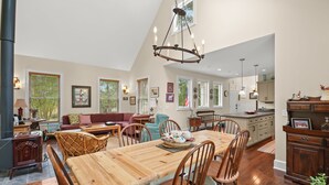 A spacious living area with a wooden dining table, comfortable seating, and a large chandelier. - Off Belay | Luxury Creekside Home, Screened Porch, Fireplace & Gourmet Kitchen (Chincoteague Island)
