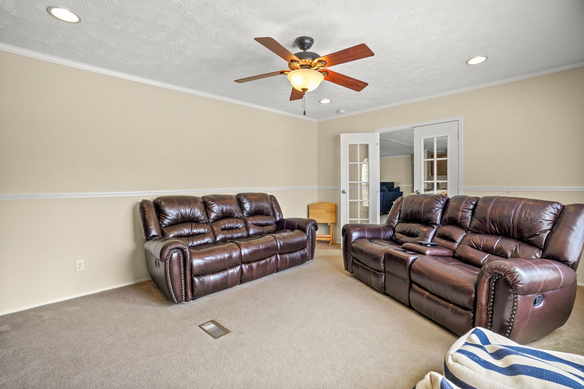 A living room with two leather sofas, a ceiling fan, and a door leading to another room.