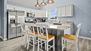 A modern kitchen with white cabinets, stainless steel appliances, and a central island with bar stools.