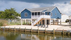 A two-story house with a balcony, a covered porch, and a dock extending into a body of water.