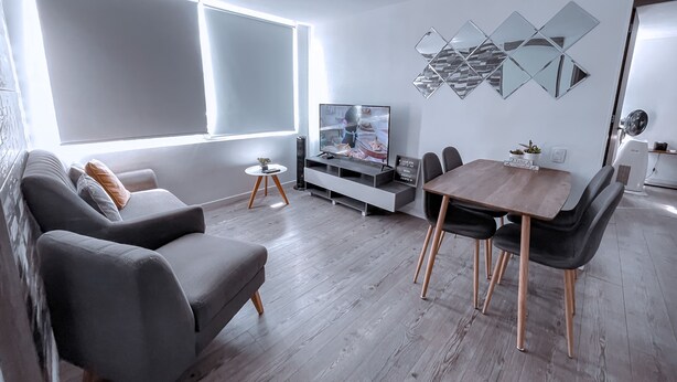 Uma sala de estar moderna com sofá, televisão, mesa de jantar e cadeiras.