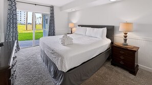 A hotel room with a large bed, two bedside lamps, a wooden nightstand, and a view of a green landscape through a sliding door.