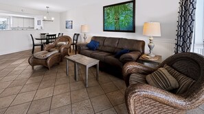 A living room with a brown leather sofa, two wicker armchairs, a small wooden coffee table, and a dining area with a white table and chairs. - El Matador 114 -  FREE TICKETS!! Your stay includes free tickets to many area attractions! (Fort Walton Beach)