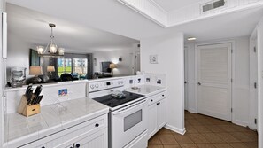 A modern kitchen with white cabinetry, a black stove top oven, and a large mirror above the countertop. - El Matador 114 - FREE TICKETS!! Your stay includes free tickets to many area attractions! (Fort Walton Beach)