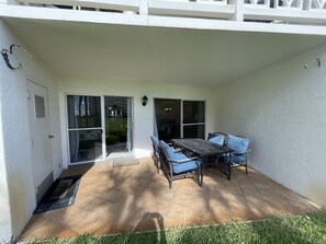 An outdoor patio with a table and chairs, a sliding glass door, and a white exterior wall.