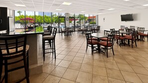 A spacious indoor area with multiple tables and chairs, large windows offering views of a pool and greenery, and a flat-screen TV mounted on the wall. - El Matador 114 - FREE TICKETS!! Your stay includes free tickets to many area attractions! (Fort Walton Beach)