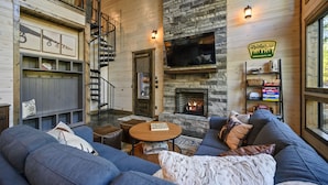 A cozy living room with a stone fireplace, a large sofa, and a wooden staircase. - Star-Spangled Fun | Arcade + Outdoor Oasis + Putt-Putt + EV Outlet (Broken Bow)