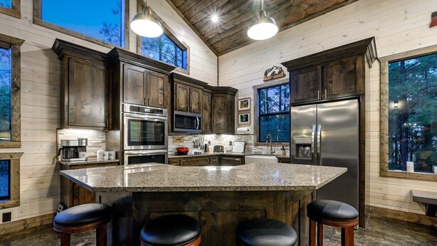 A spacious kitchen with dark wooden cabinets, stainless steel appliances, and a large granite island with bar stools. - Star-Spangled Fun | Arcade + Outdoor Oasis + Putt-Putt + EV Outlet (Broken Bow)