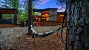 Une cabane moderne avec une façade en pierre, un hamac et une terrasse en bois.