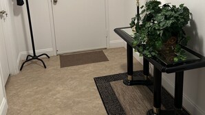 Un pasillo con perchero, puerta, lámpara, planta en maceta y alfombra.