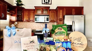 Una cocina con armarios de madera, un refrigerador de acero inoxidable y un microondas. Hay bolsas de regalo, una botella de licor y alimentos en la encimera.