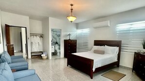 Un dormitorio amplio con una cama grande, un sofá y un baño que se aprecia al fondo.