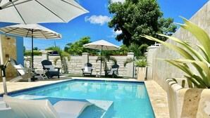Una piscina con sillas de descanso y sombrillas, rodeada de muros de piedra y vegetación.