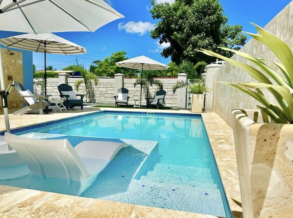 A swimming pool with lounge chairs and umbrellas, surrounded by stone walls and greenery.